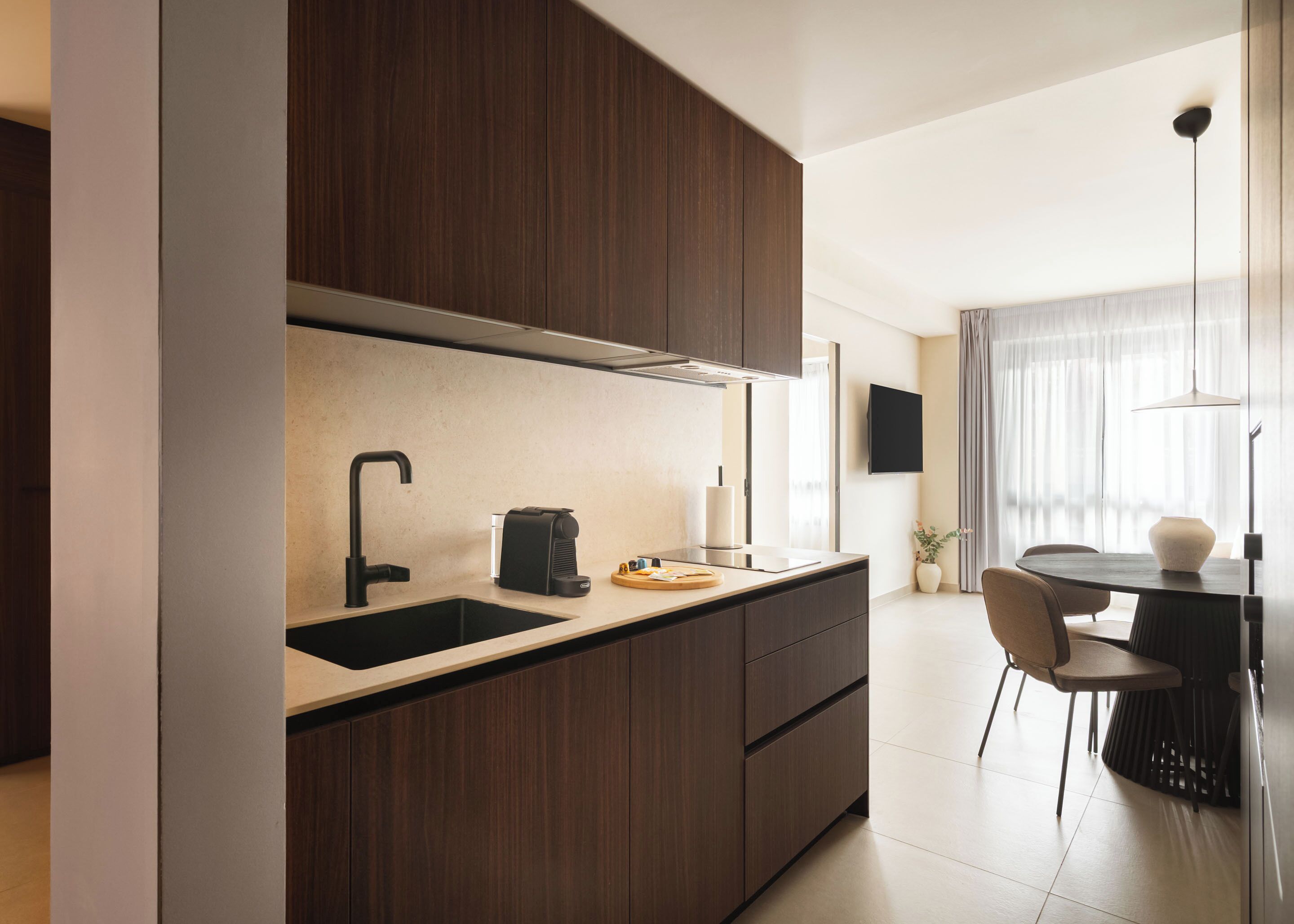 A modern kitchen with a built-in sink, a coffee machine, and a dining area with a table and chairs.