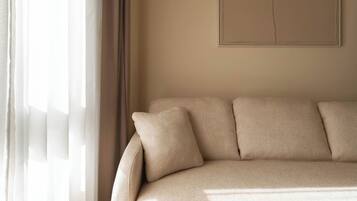 A minimalist living room with a beige sofa, sheer curtains, and a simple wall-mounted artwork.