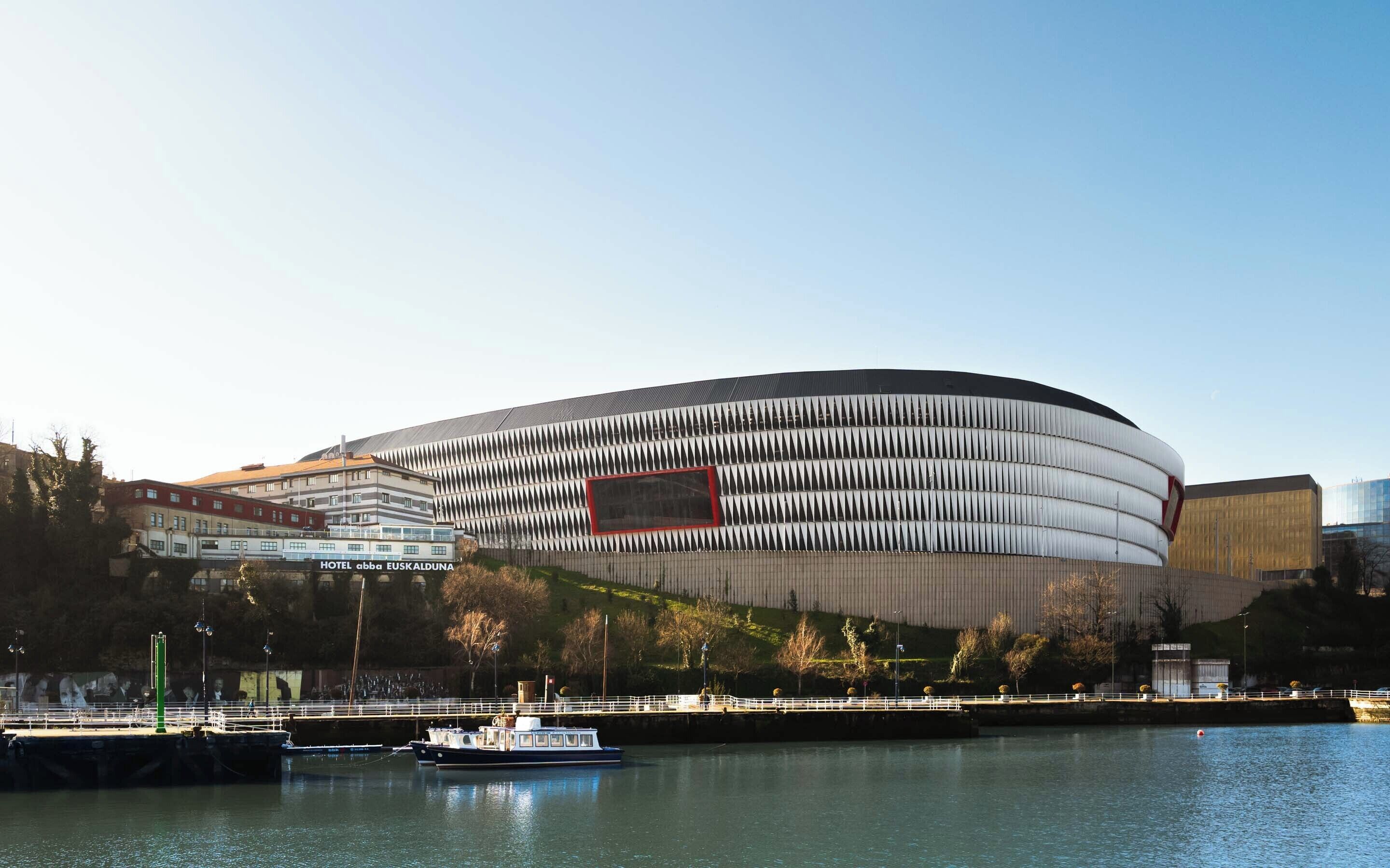 A modern hotel with a distinctive curved facade, situated by a waterfront with a boat dock.