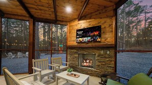 Ein gemütliches Blockhauss-Interieur mit Kamin aus Stein, Holzmöbeln und großen Fenstern mit Blick auf einen Wald.