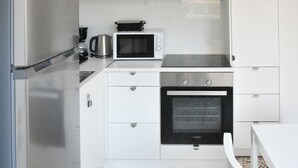Une cuisine moderne équipée d’un réfrigérateur en acier inoxydable, d’un four à micro-ondes, d’un four encastré et de meubles de rangement blancs.