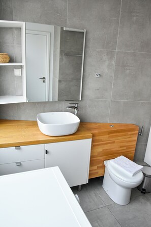 Un baño moderno con un lavamanos blanco, tocador de madera y un inodoro blanco.