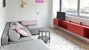 Un salon moderne avec un canapé gris, une petite table ronde et un meuble de rangement rouge pour les appareils électroniques.