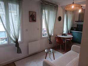 Ein modernes Wohnzimmer mit einem weißen Sofa, einem Glastisch und einem Essbereich mit einem roten Sessel und einem kleinen Tisch.