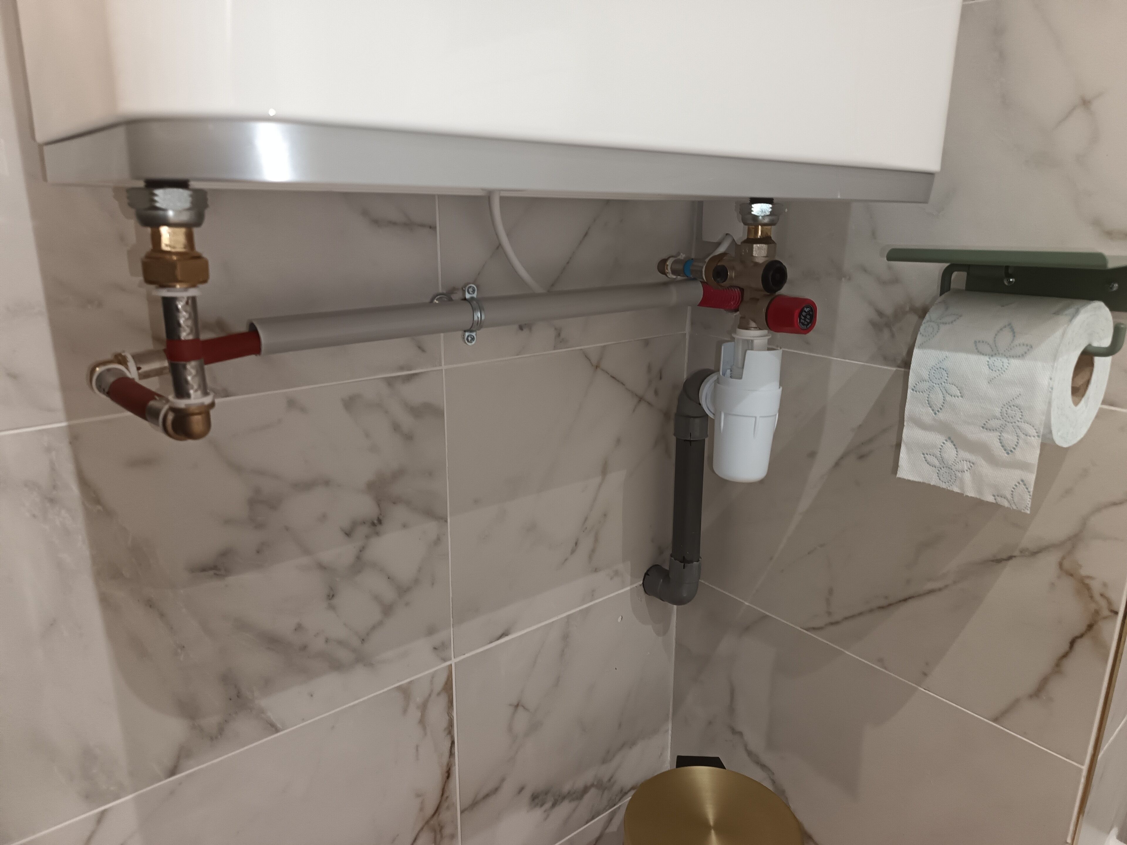 Een badkamer met marmeren tegels, een toiletrolhouder en zichtbare sanitaire voorzieningen.