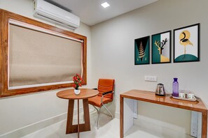 A room with a large window, a round table with a vase of flowers, an orange chair, a wooden desk with a kettle and a water bottle, and three framed artworks on the wall. - Collection O Aiims Bhubaneshwar (Bhubaneshwar)
