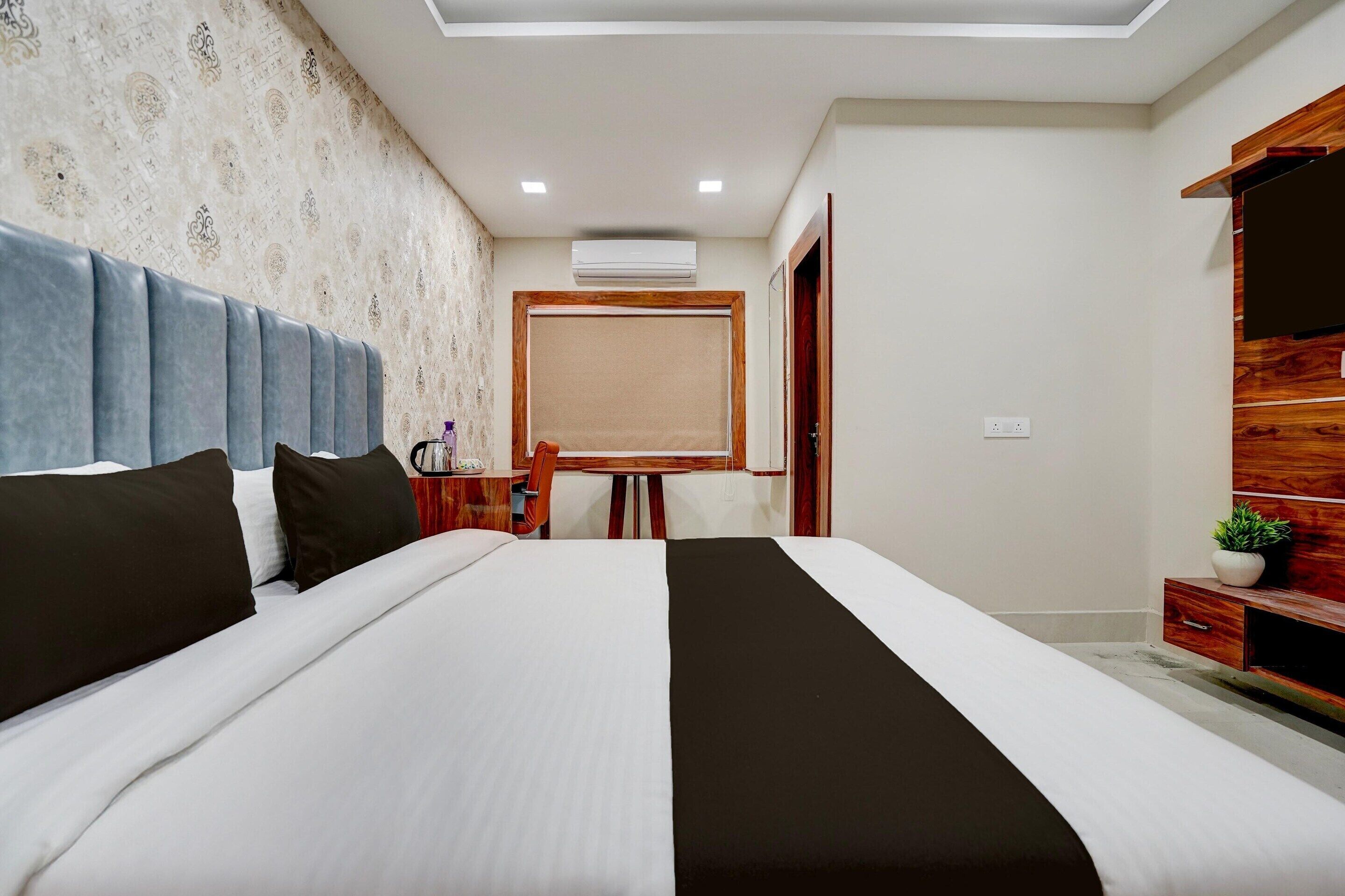 A hotel room with a large bed, a desk with a chair, a wardrobe, and a door leading to another room.