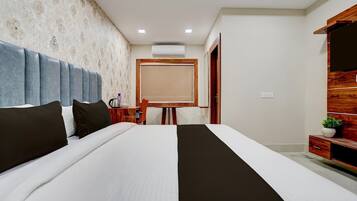 A hotel room with a large bed, a desk with a chair, a wardrobe, and a door leading to another room.