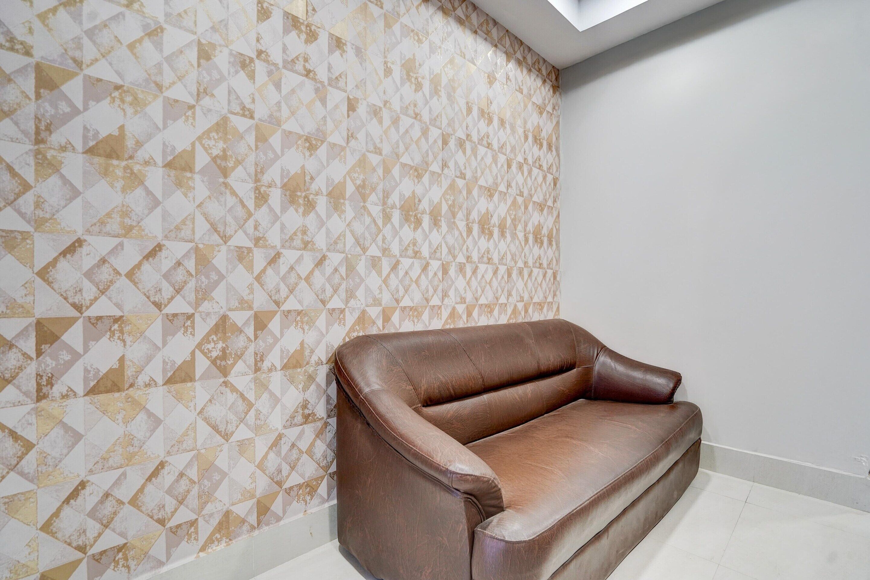 A brown leather sofa against a wall with a geometric patterned wallpaper.