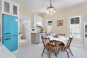Une cuisine avec un réfrigérateur bleu, des chaises en bois disposées autour d’une table et un lustre.