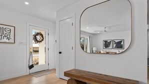 Un intérieur moderne avec un banc en bois, un grand miroir et une porte donnant sur un espace extérieur.
