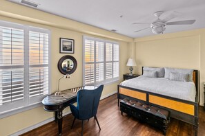 A bedroom with a bed, a desk, a chair, a ceiling fan, and large windows with blinds. - New! Beachfront Condo, Fishing / Pool / Boat (Virginia Beach)