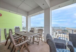 A covered outdoor patio with a wooden table and chairs, a wicker sofa, and a view of the beach. - New! Beachfront Condo, Fishing / Pool / Boat (Virginia Beach)