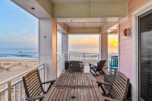 A wooden deck with a table and chairs, overlooking a beach with a sunset view. - New! Beachfront Condo, Fishing / Pool / Boat (Virginia Beach)