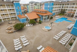 A hotel courtyard with multiple swimming pools, lounge chairs, and a central fountain. - New! Beachfront Condo, Fishing / Pool / Boat (Virginia Beach)