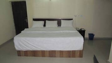 Quarto de hotel com uma cama grande, cabeceira de madeira, mesa de cabeceira com telefone e uma lixeira azul.
