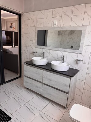 A bathroom with two sinks, a large mirror, and a toilet. - Castle Rock Guest House  (Bulawayo)