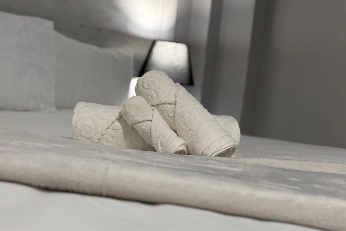 A neatly made bed with rolled white towels.