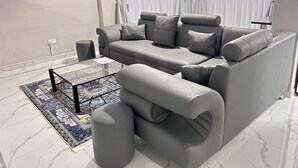 A modern living room with a grey sofa, ottoman, and a glass coffee table with a patterned rug. - Castle Rock Guest House  (Bulawayo)