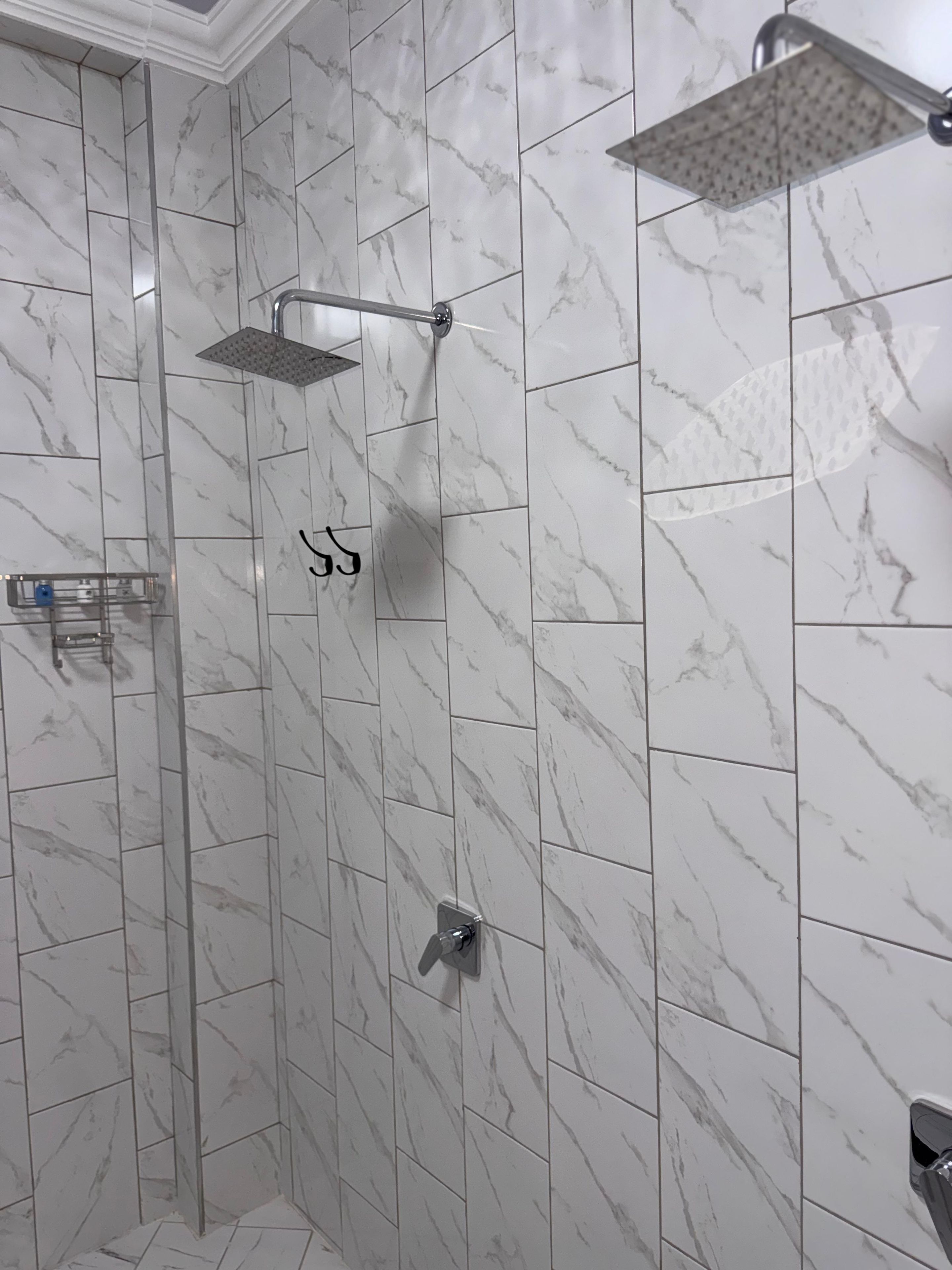 A shower area with a rain showerhead and a handheld showerhead mounted on the wall.