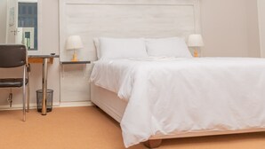 A bedroom with a bed, two bedside tables with lamps, a chair, a small table, and a curtain. - Castle Rock Guest House  (Bulawayo)