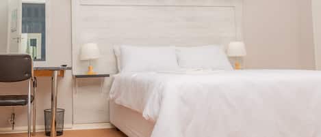 A bedroom with a bed, two bedside tables with lamps, a chair, a small table, and a curtain.