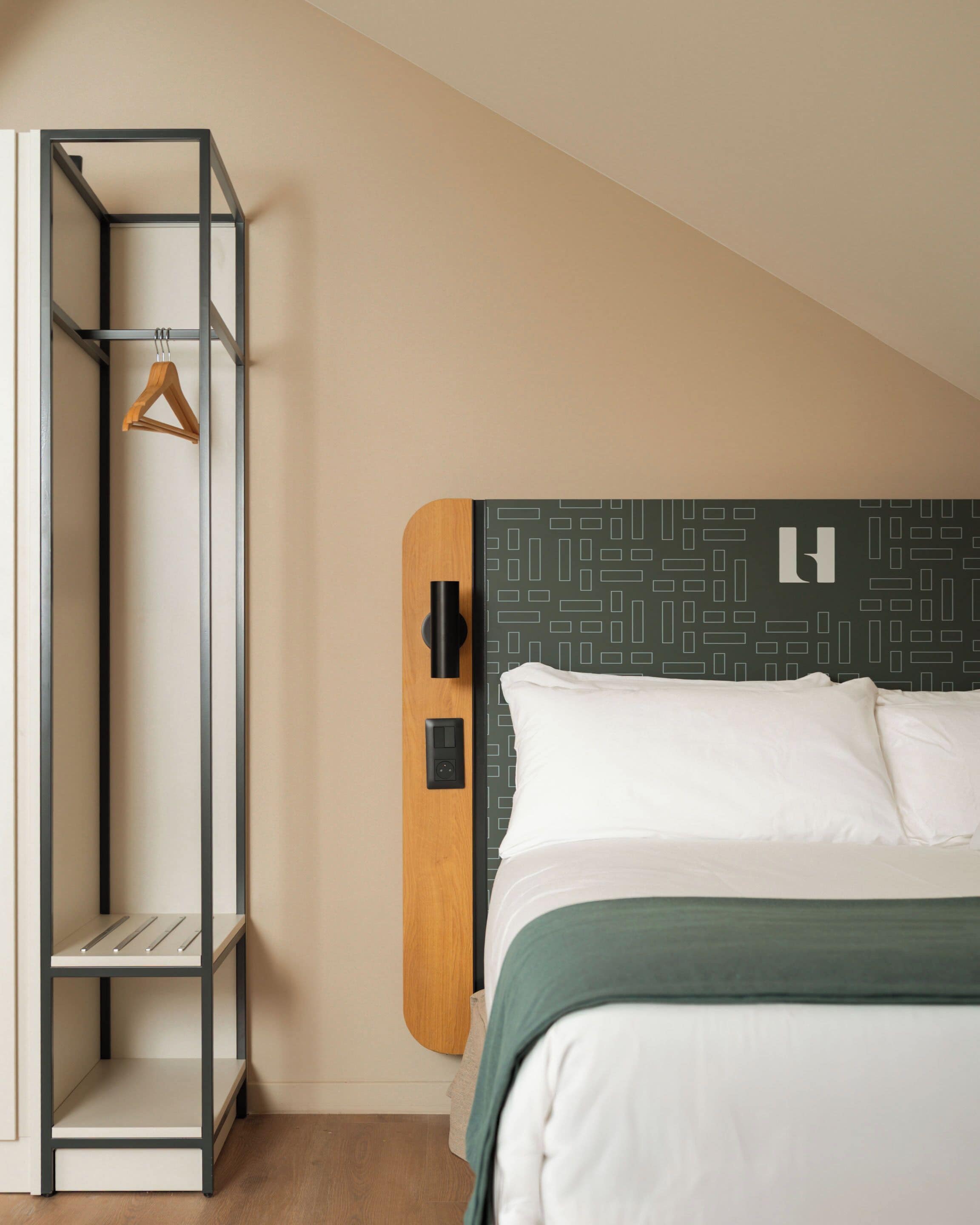 A bedroom with a bed, a wooden headboard, a metal shelving unit, and a hanging garment.