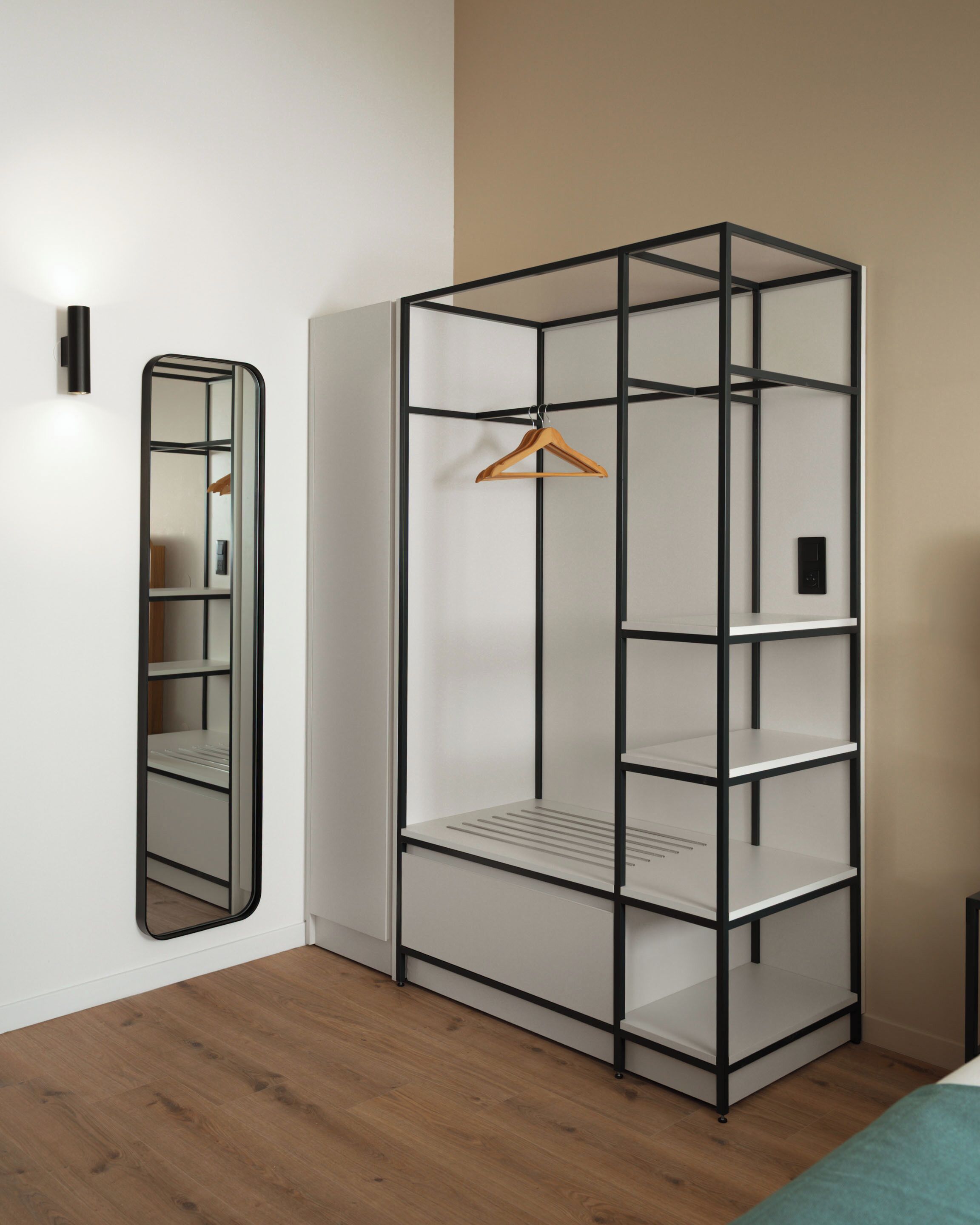 Una habitación con un armario metálico negro, un espejo y suelo de madera.