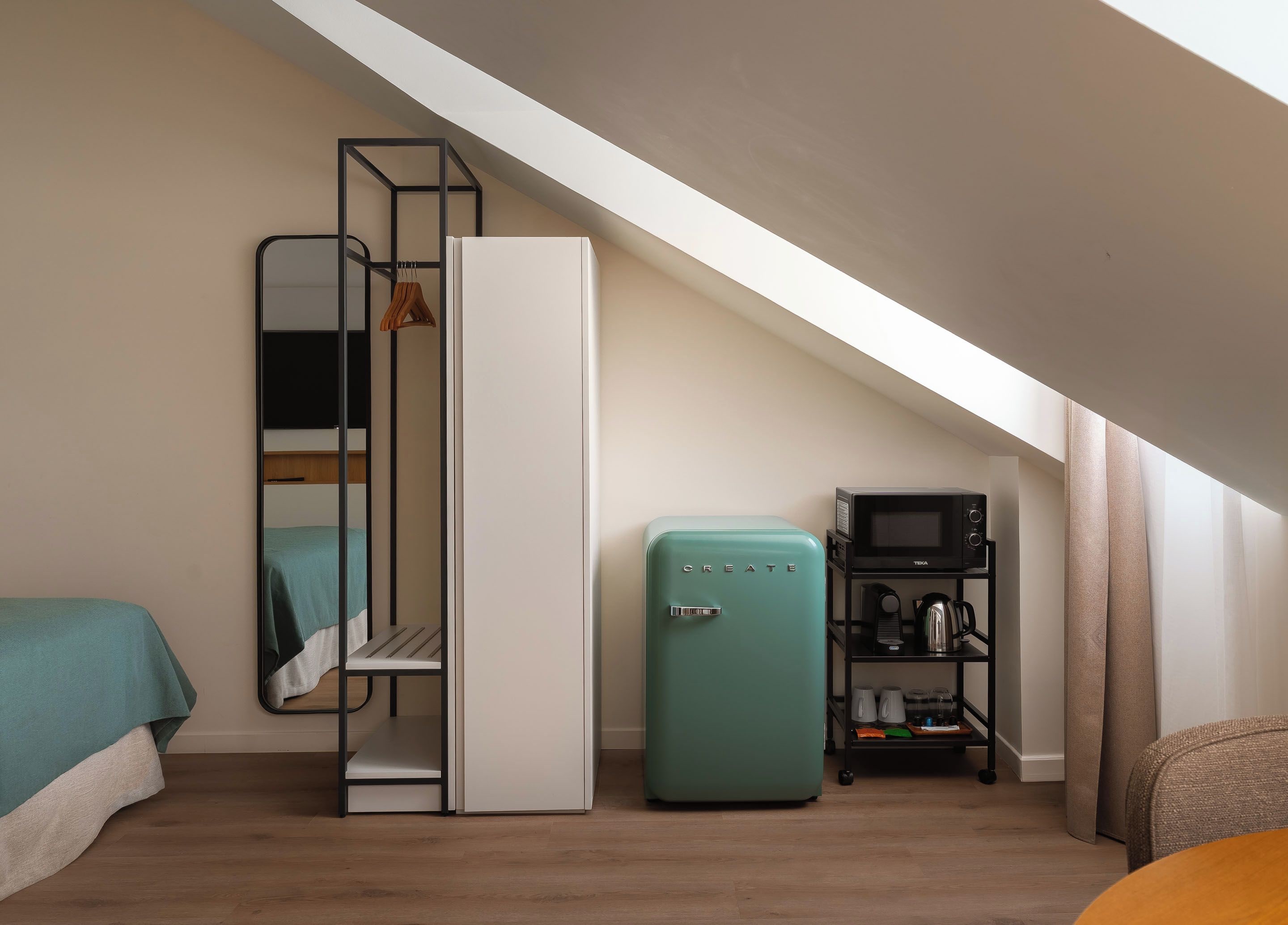 A compact room with a bed, a wardrobe, a kitchenette, and a television.