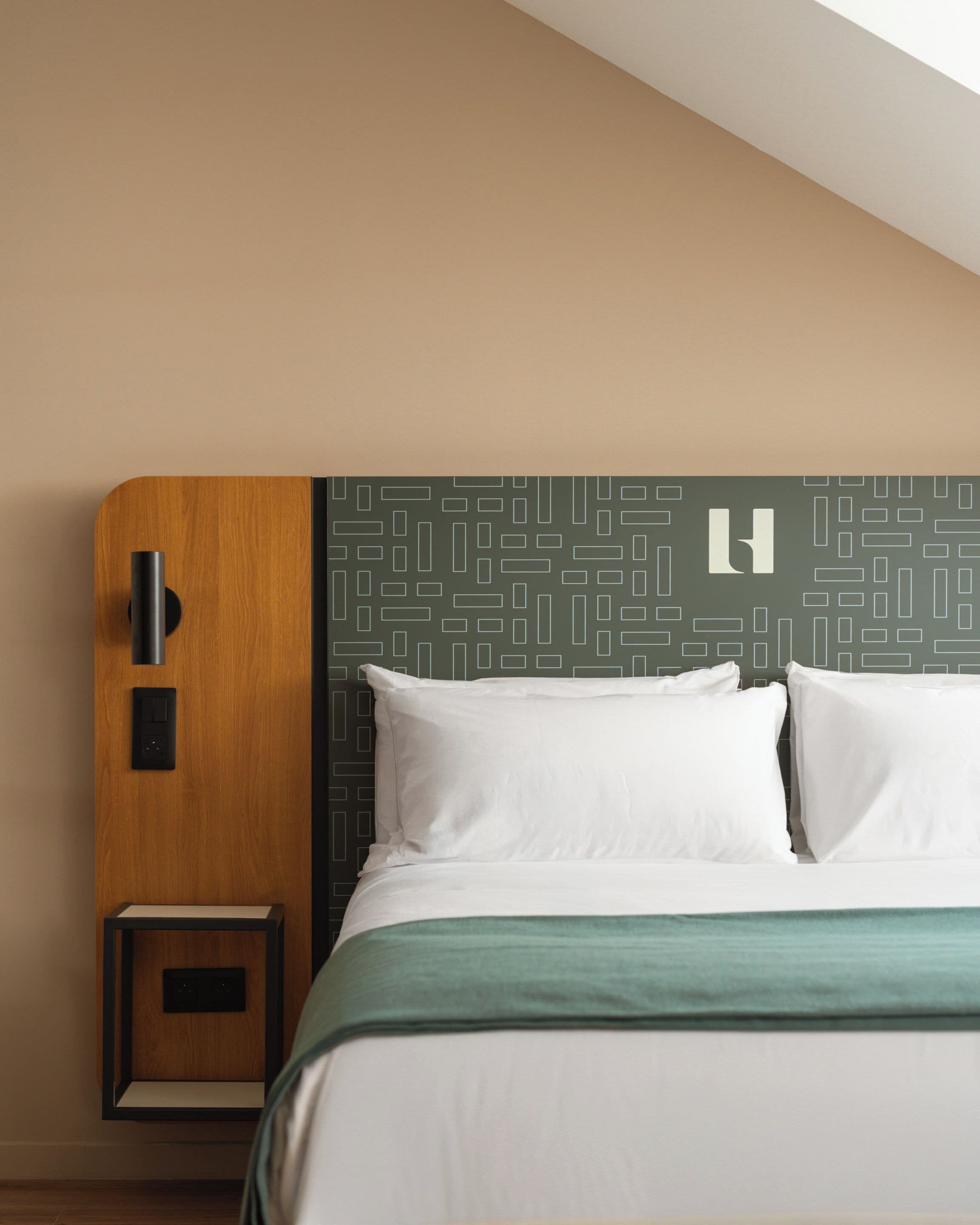 Una habitación de hotel con cama, mesita de noche, panel de control en la pared y cabecero con estampado geométrico.