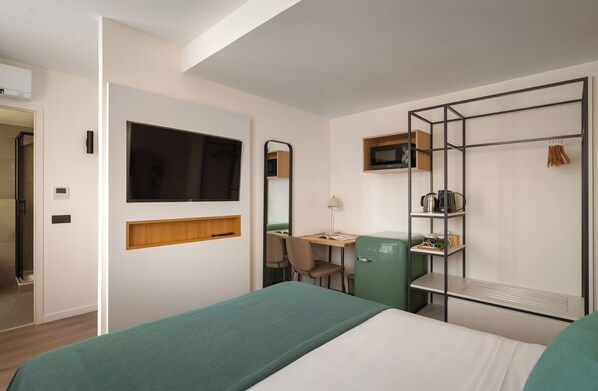 A hotel room with a bed, a desk with a chair, a television, a microwave, and a wardrobe. - Limehome Versailles Rue du Bailliage (Versailles)