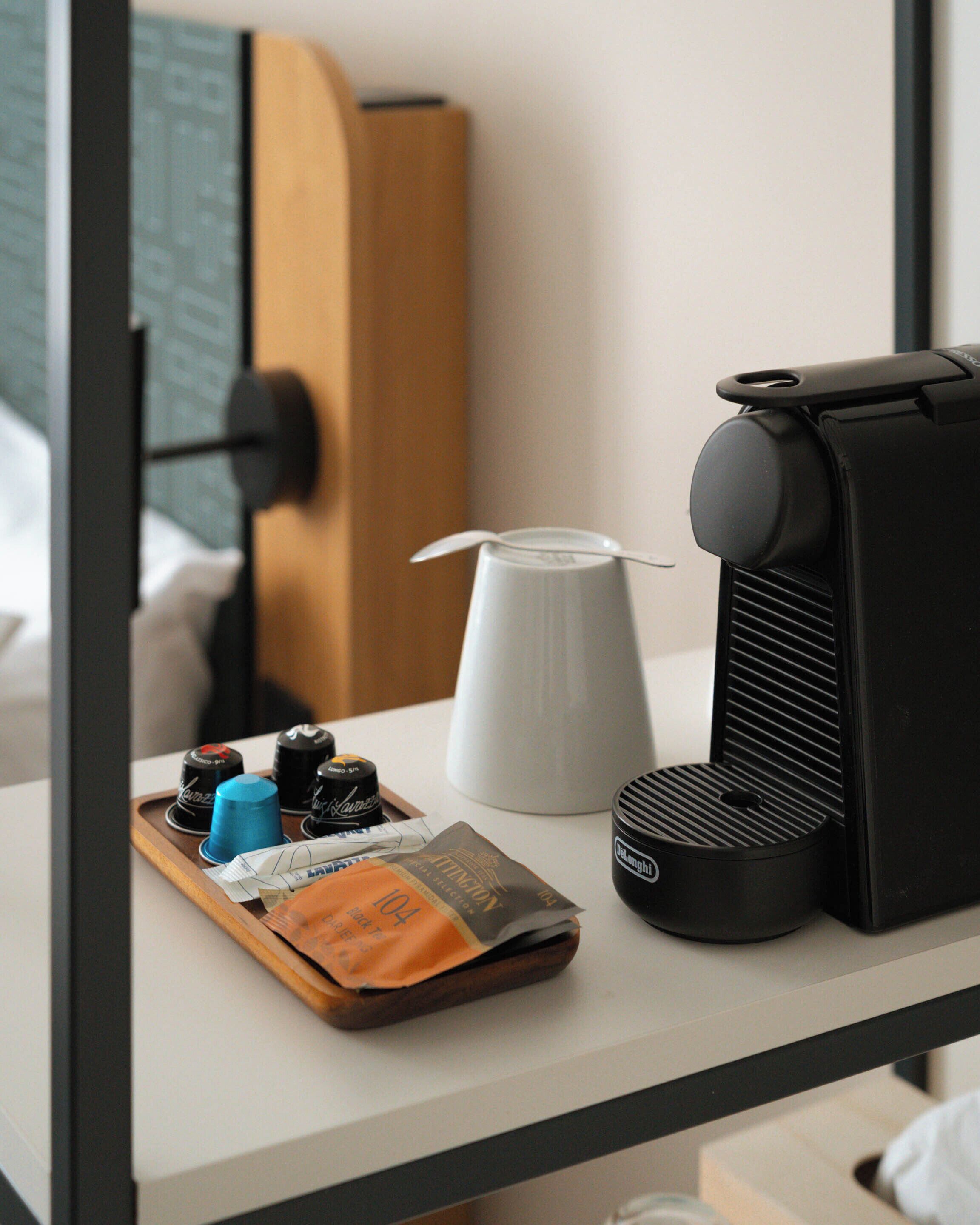 Une machine à café, une tasse blanche et un plateau contenant des dosettes de café et un paquet, le tout posé sur une table d’hôtel.