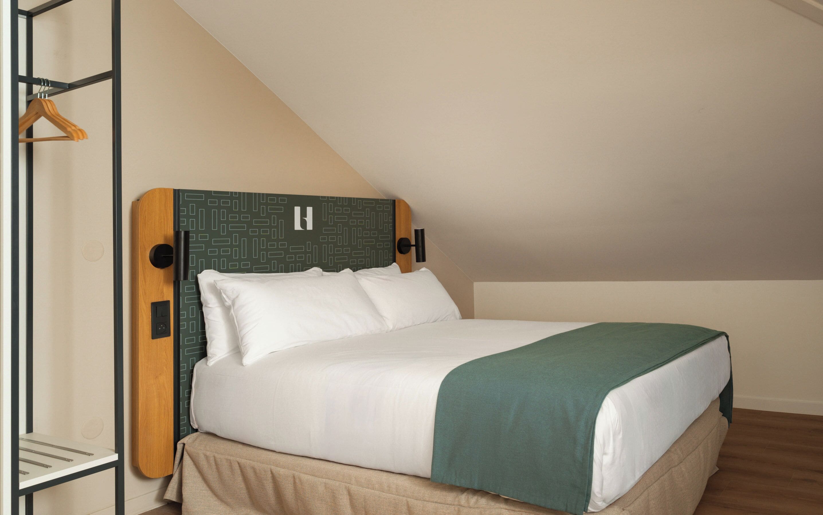 A single bed with a wooden headboard, white bedding, and a green throw blanket.
