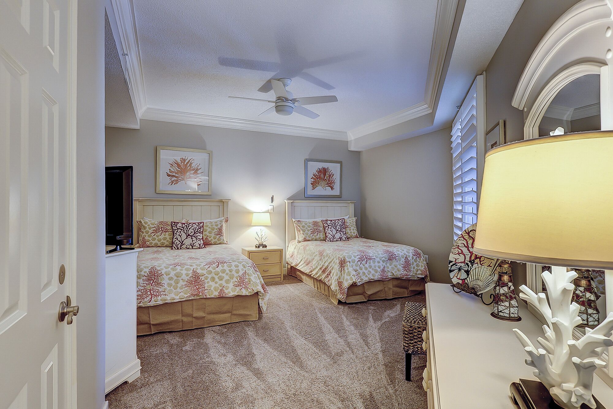 A bedroom with two beds, a ceiling fan, a TV, and a lamp.