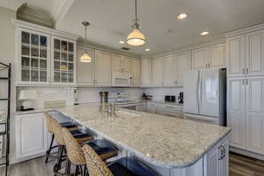 A kitchen with white cabinets, a granite countertop, a stainless steel refrigerator, and pendant lighting. - 3205 Seacrest – Oceanfront Corner Villa with Panoramic Atlantic Views (Hilton Head Island)