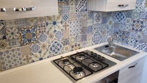 Een keuken met een gasfornuis, een spoelbak en betegelde spatwand.