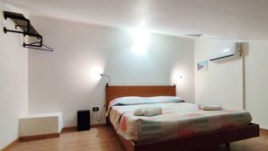 Een enkel bed in een kamer met een houten vloer, een witte muur en een plafondlamp.