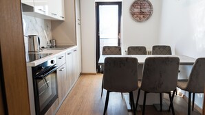 Een kleine keuken met een inbouwoven, een eettafel met vier stoelen en een wandklok.
