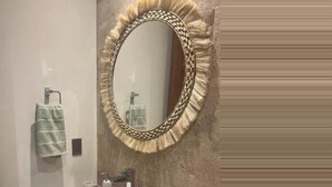 Un baño con un espejo redondo, tocador de madera y lavamanos.