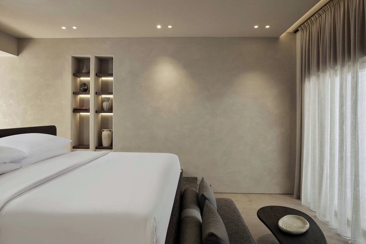 A modern hotel room with a large bed, built-in shelves, and a view of the outdoors.