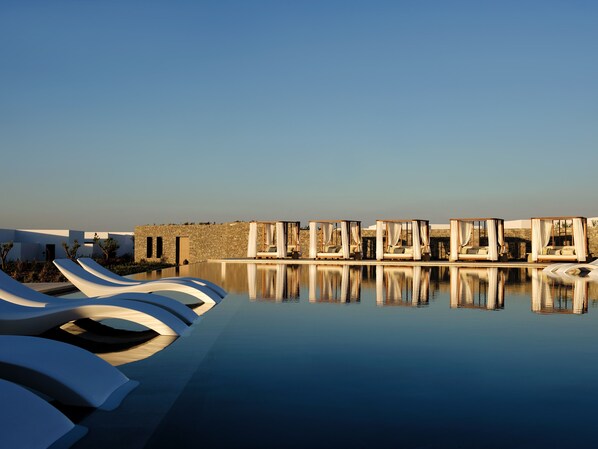 Un espace piscine paisible, doté de chaises longues modernes et de lits à baldaquin, qui reflète la clarté du ciel.