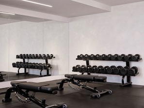 Ett gym med ställningar för vikter, bänkar och en vägg med speglar.
