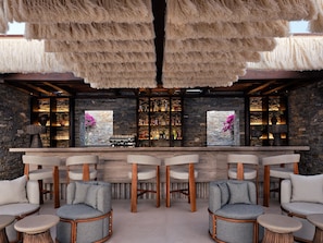 A bar area with stone walls, wooden furniture, and a thatched ceiling.