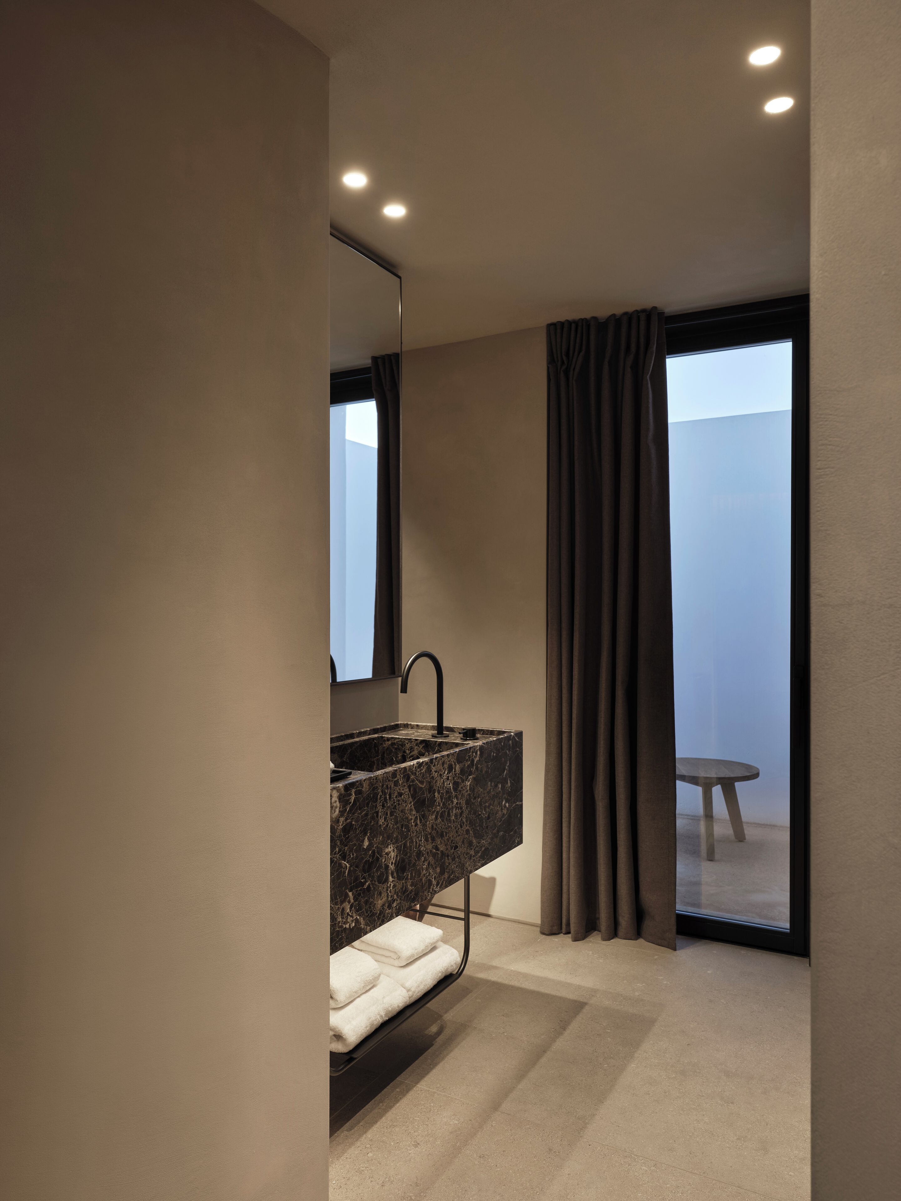A modern bathroom with a marble sink, a mirror, and a view of a balcony.