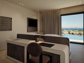 Une chambre d’hôtel moderne équipée d’un lit, d’un bureau avec une chaise, d’un téléviseur à écran plat et d’une grande fenêtre offrant une vue sur la mer et les montagnes.