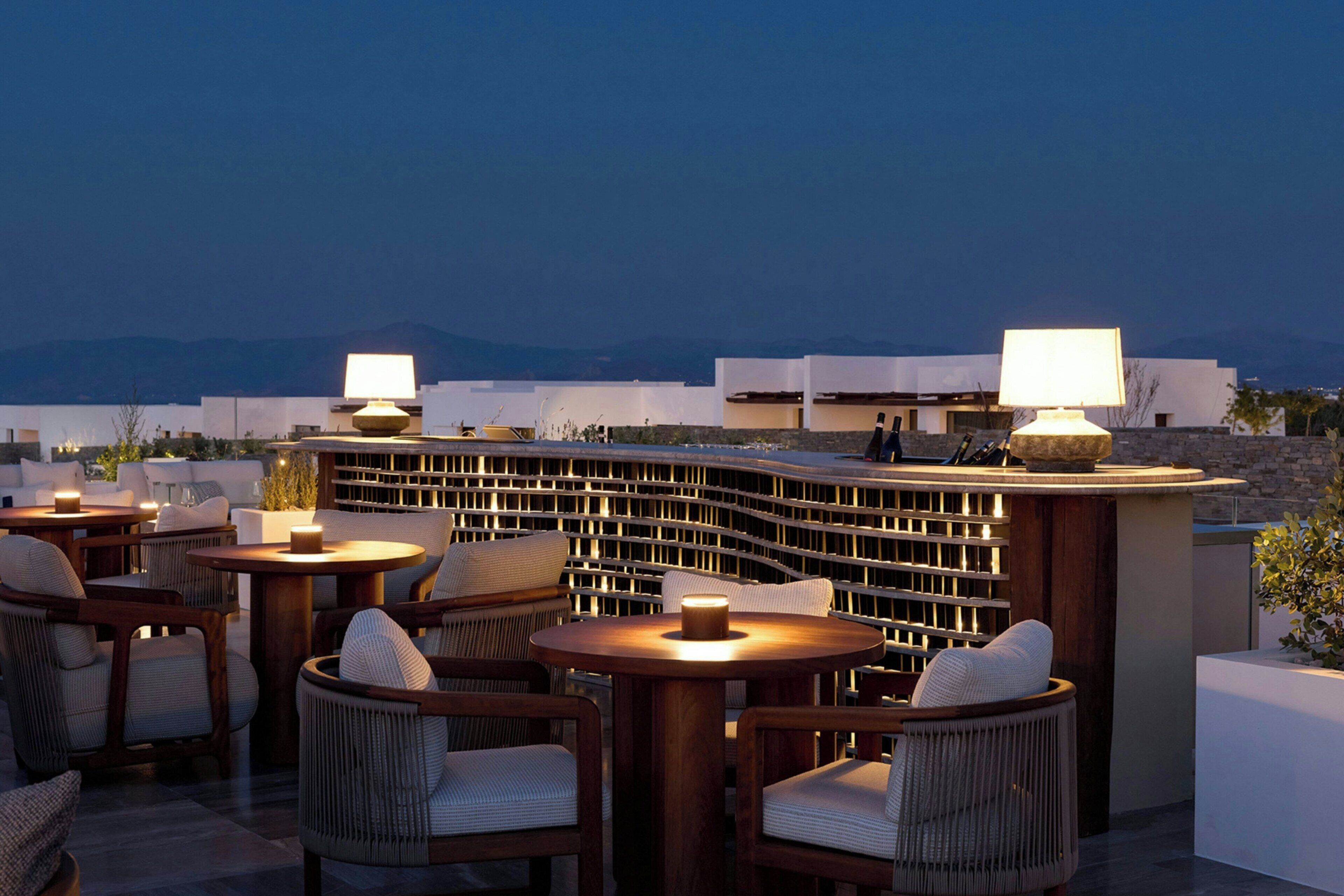 An outdoor seating area with round tables and chairs, a decorative wall, and a view of the mountains in the background.
