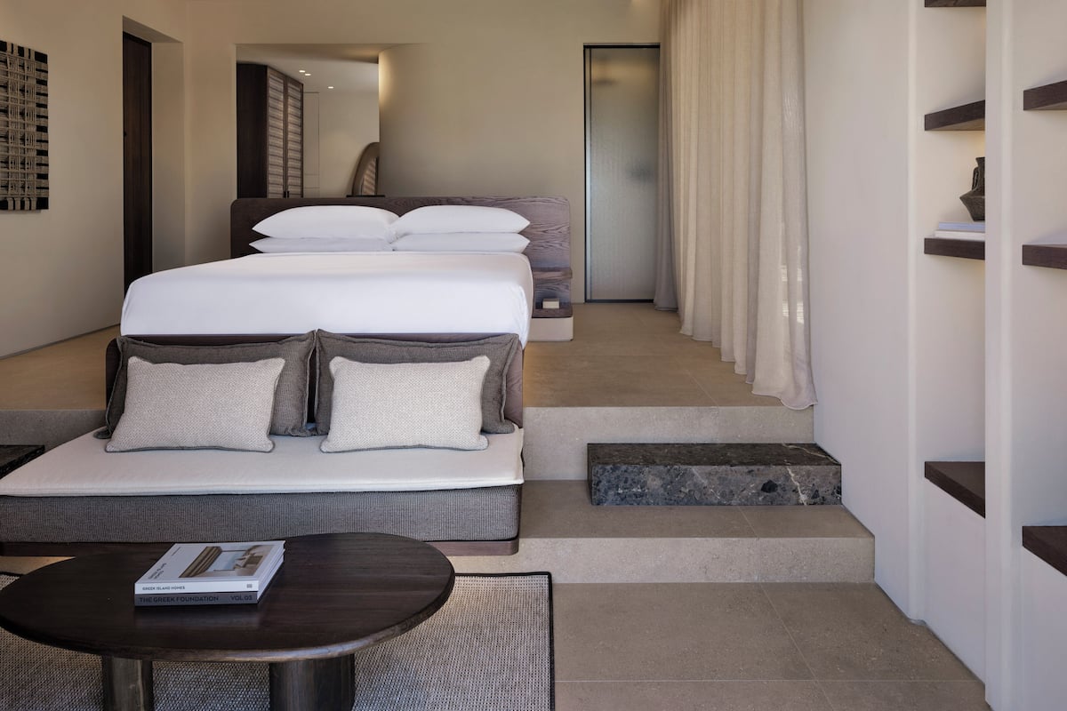 Habitación de hotel moderna con una cama grande, un pequeño sofá, una mesa redonda y una escalera que lleva a otra habitación.