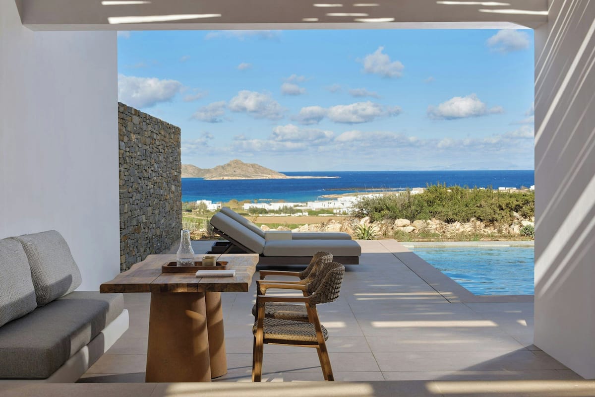 A modern outdoor seating area with a pool, stone wall, and a view of the sea.