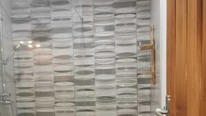 Eine Dusche mit einem geometrischen Fliesenmuster, eine Holztür und eine weiße Toilette.