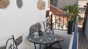 Eine kleine Außenveranda mit zwei runden Tischen und Stühlen, einem Blumentopf und einem dekorativen Metallgeländer.